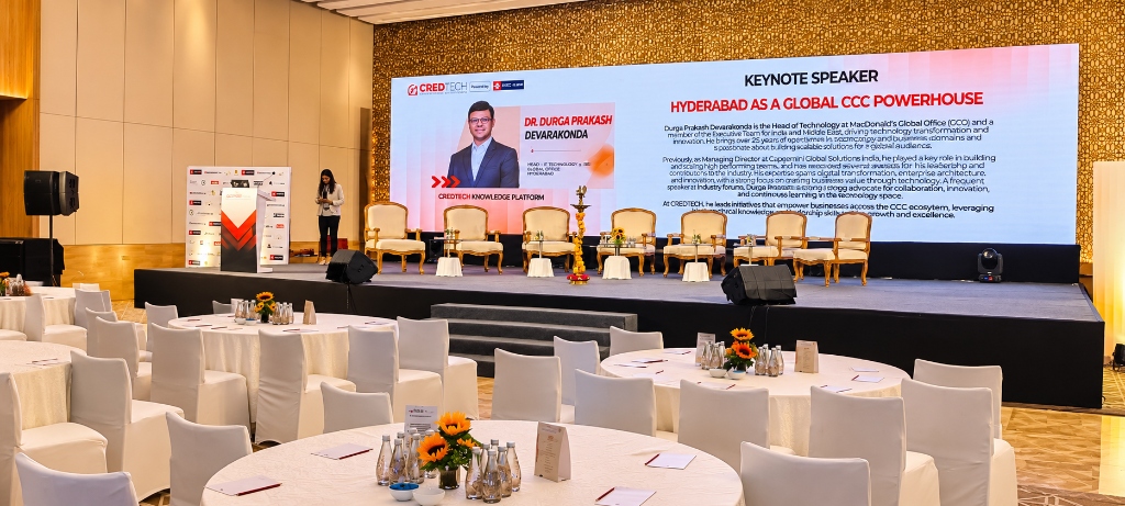 Jaya Media CredTech leadership summit stage with large LED screen, keynote speaker podium, and round banquet tables